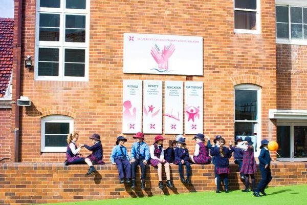 St Andrews Catholic Primary School Malabar - students sitting on bench in front of schools banners